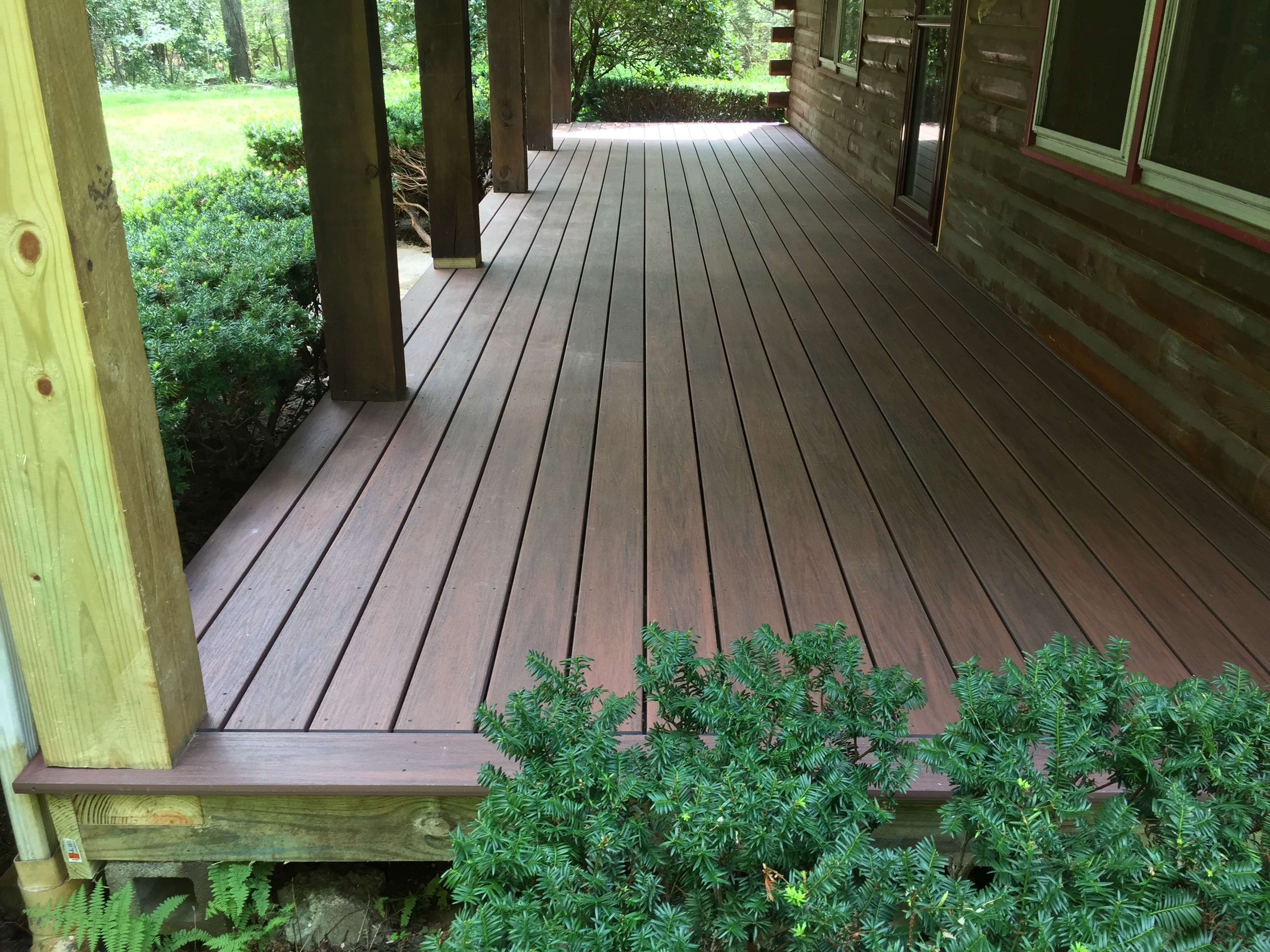 Completed deck reframe — new Trex mahogany composite decking on log home porch, reframed structure with covered post bases, Eastern Connecticut