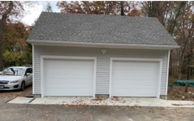 Completed two-car detached garage — white vinyl siding, two white overhead doors, gray architectural shingles, new concrete apron, fall foliage Eastern Connecticut
