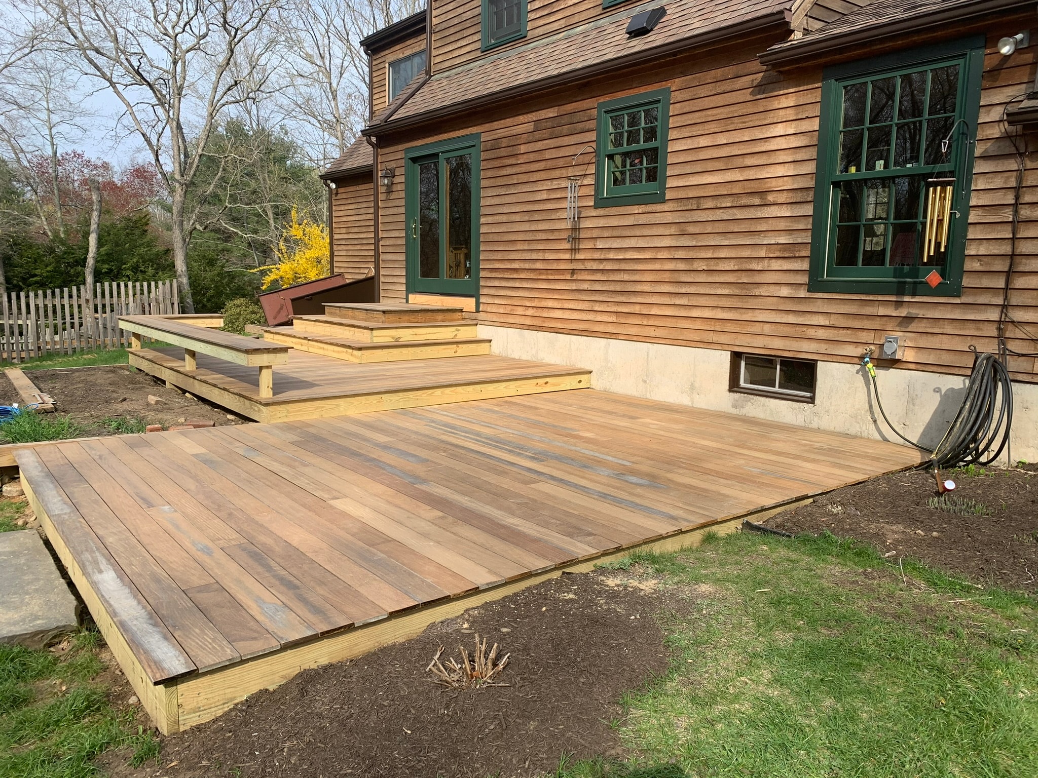 Salvaged replaned mahogany decking reinstalled on new pressure-treated framing — wide view of completed lower deck level with built-in bench and upper landing, cedar colonial home