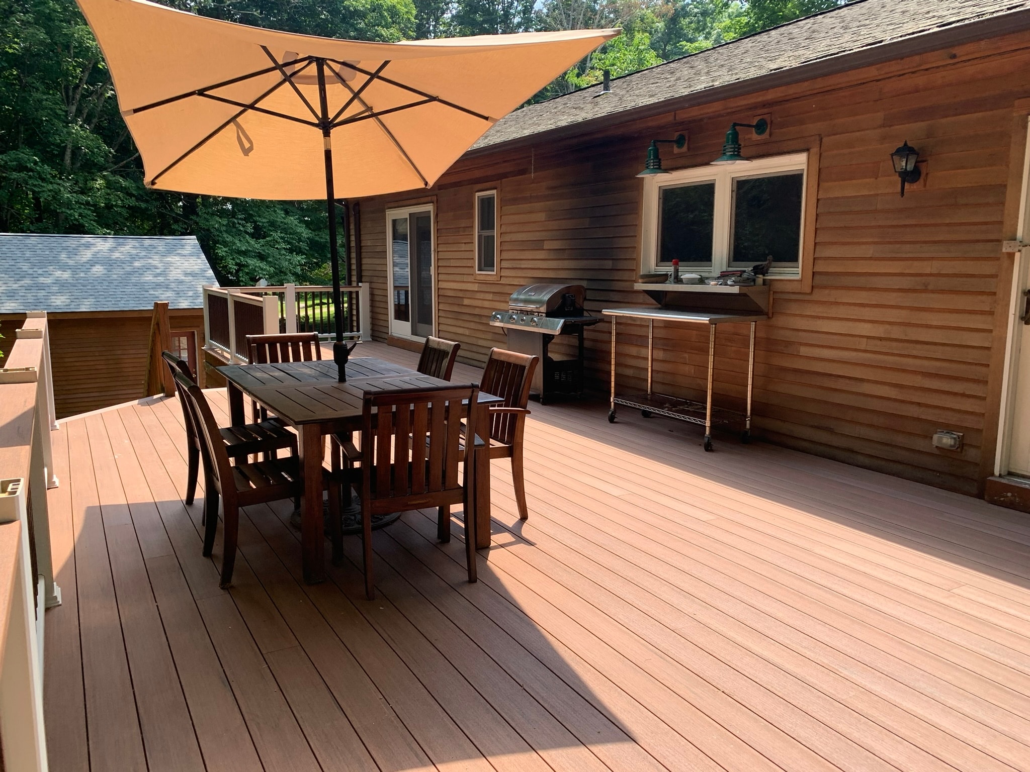 Completed Trex composite deck with dining set and orange umbrella — new cedar-tone decking and white railing kits installed on cedar-sided home, Eastern Connecticut