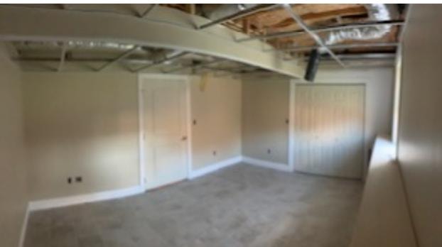 Finished basement great room — large open space with tile floors, custom built-in shelving units on both walls, open doorway to adjacent room, unfinished drop ceiling grid, Eastern Connecticut