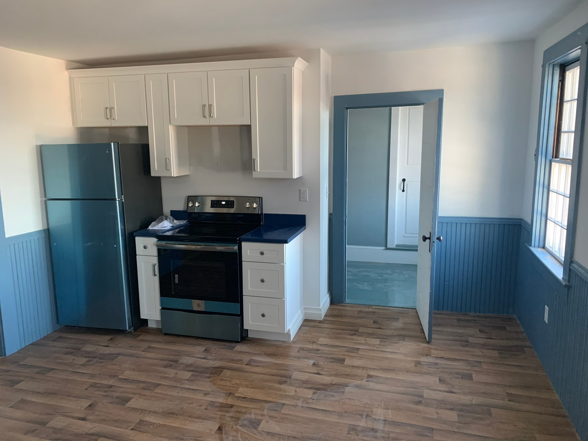 Kitchen remodel detail — blue beadboard wainscoting, white upper cabinets, dark laminate countertop, and new vinyl plank flooring, Eastern Connecticut