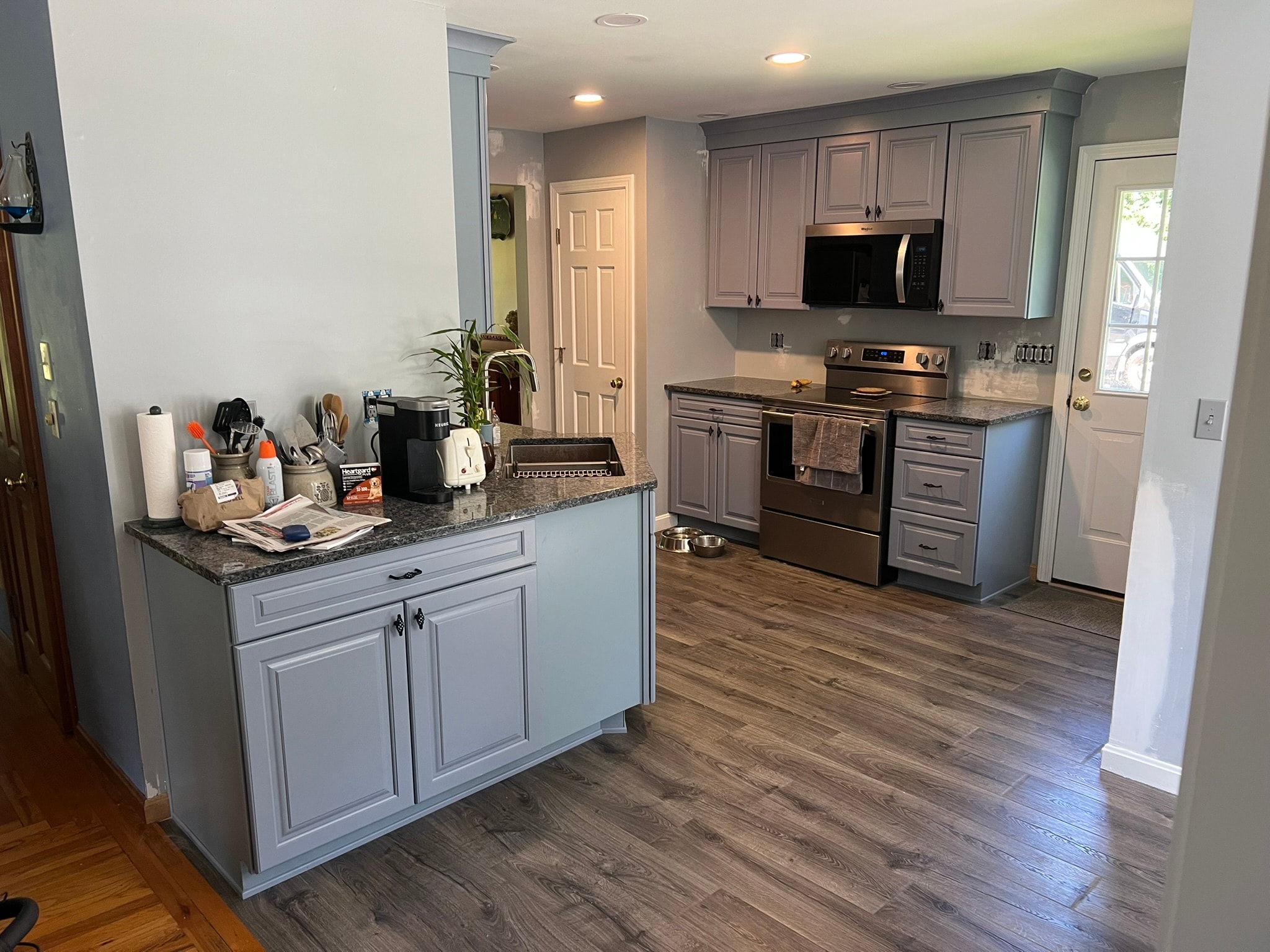 Completed kitchen remodel — blue-gray raised-panel cabinets with crown molding, dark granite countertops, Whirlpool stainless range and over-range microwave, new LVT flooring — Eastern Connecticut