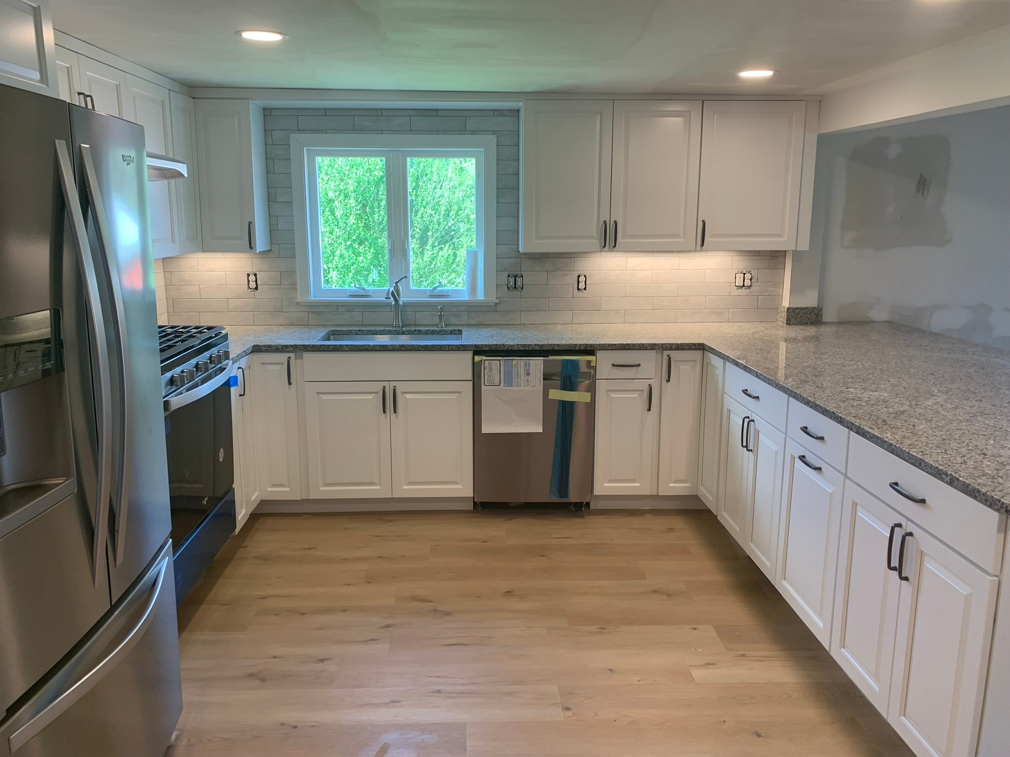 Kitchen sink wall — white shaker cabinets, subway tile backsplash, granite countertops, and garden window with under-cabinet lighting