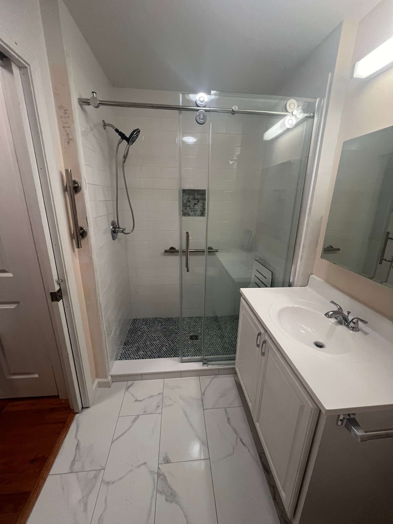 Completed bathroom remodel — custom walk-in shower with sliding glass door, penny tile floor, white subway tile walls, and marble-vein porcelain floor tile with aligned veining