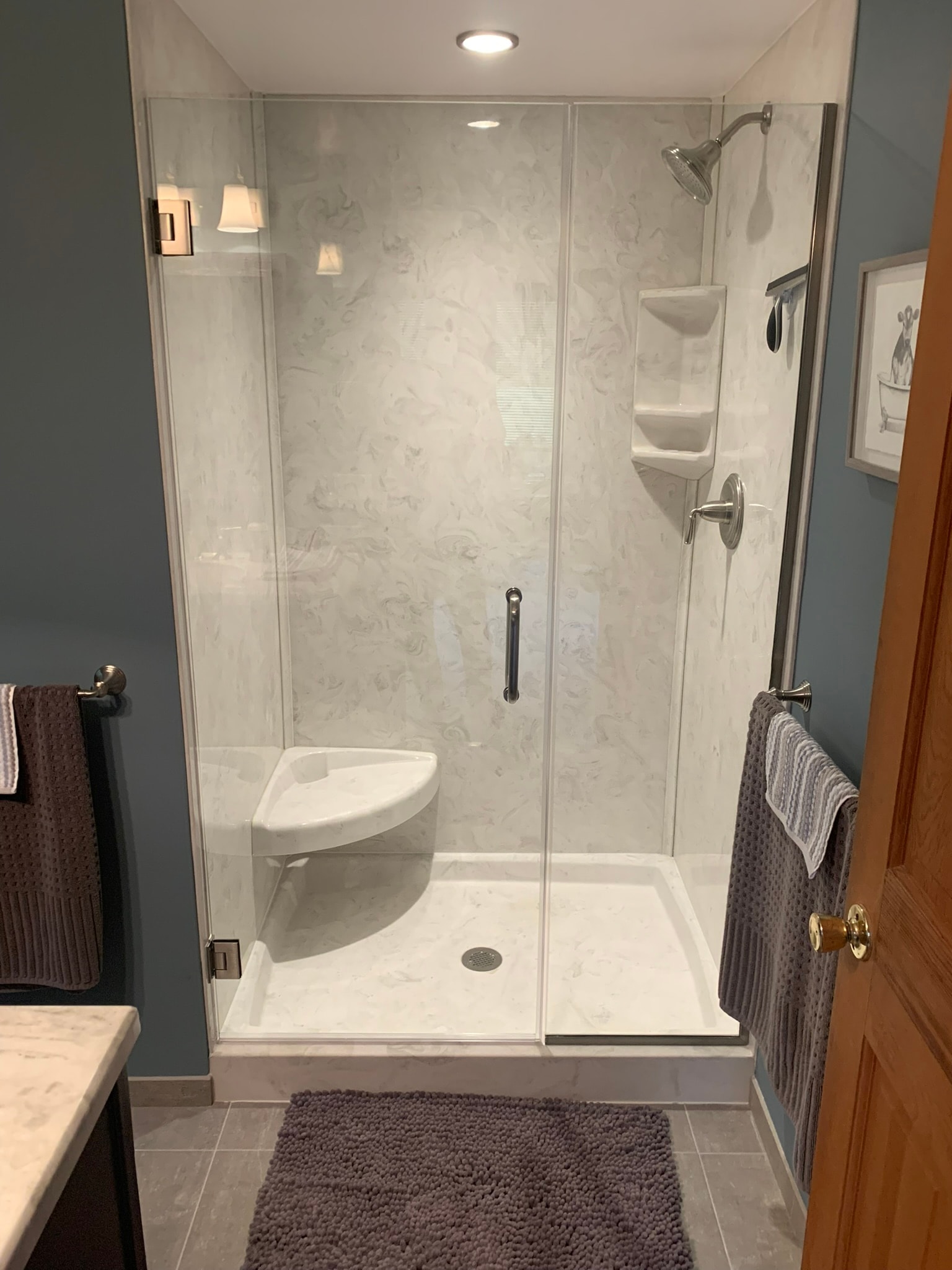 Synmar fiberglass shower stall with marble-look walls, corner seat, glass door, and new tile floor