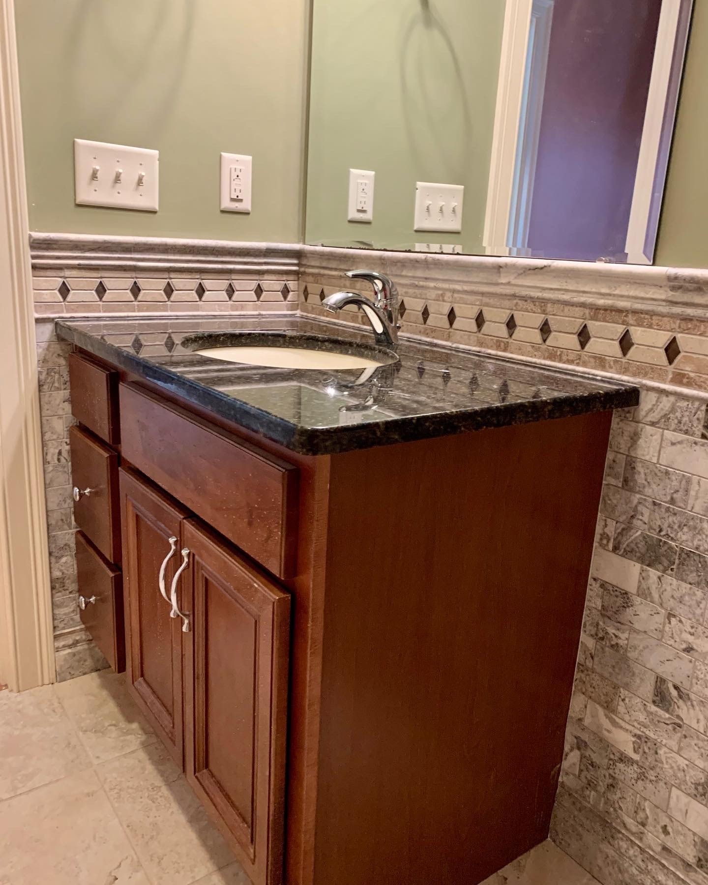 Tiled wainscotting with dark granite vanity and diamond border trim