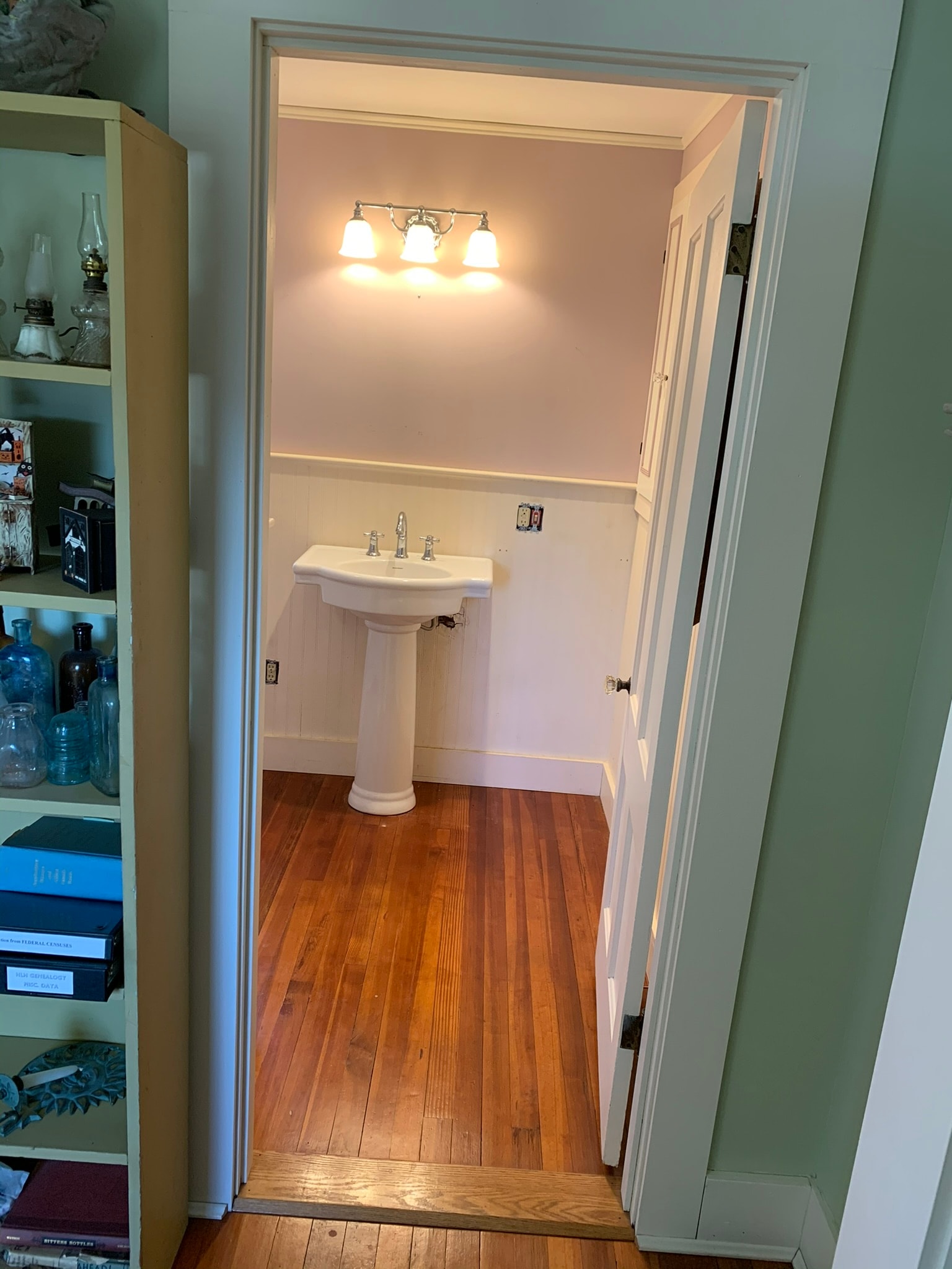 Newly created Victorian bathroom — pedestal sink, three-light vanity fixture, and original hardwood floors